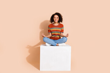 Sticker - Full size photo of relaxed nice woman wear knit t-shirt denim pants sit on cube in meditation pose isolated on beige color background