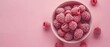   A white bowl sits atop a pink surface, brimming with raspberries Surrounding the bowl are additional raspberries