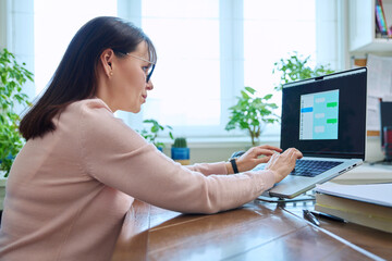 Middle-aged woman communicates online using laptop at desk at home
