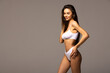 Portrait of tender young woman with perfect body shape posing in beige cotton underwear over grey background.