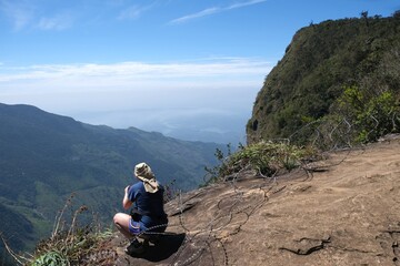 Wall Mural - Beautiful scenery of Horton Plains National Park in Nuwara Eliya, Sri Lanka. Silhouette of sitting woman on viewpoint named End of World.