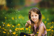 A cute little girl wearing headphones blowing dandelion fluff.