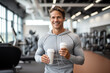 Portrait of smiling sporty man holding plastic cup of coffee in gym