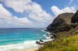 a beautiful spring landscape along the coast of Oahu with a sandy beach, blue ocean water, majestic mountain ranges, lush green trees and plants, rocks, blue sky and clouds in Honolulu Hawaii USA