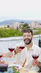 Wall Mural - Young group of millennial people toasting red wine at home party celebration. Multiracial friends sitting around dinner table while enjoying barbecue at weekend. Summer lifestyle concept.