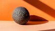   Avocado on table before orange wall, casts shadow ..Or: An avocado sits on a table, facing an orange wall; its shadow is