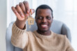 A cheerful man proudly presents a set of keys with a house-shaped keychain, symbolizing new homeownership. His smile reflects the joy and accomplishment of acquiring a new home. Man Holding House Keys