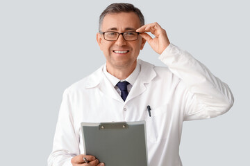 Poster - Mature doctor in eyeglasses with clipboard on light background