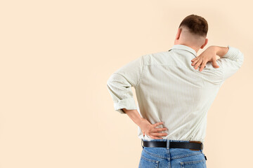 Wall Mural - Young man suffering from back pain on beige background