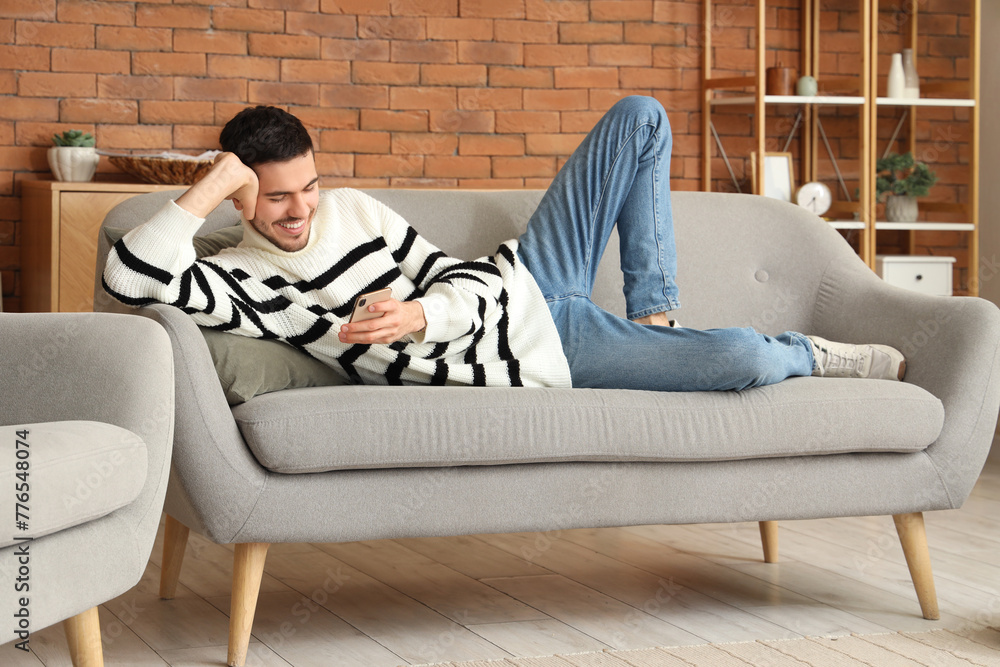 Handsome young happy man with mobile phone resting on sofa at home