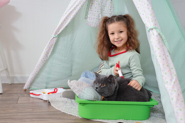 Sticker - Cute little girl with first aid kit giving injection to her British cat in hovel at home