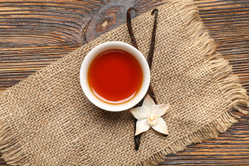 Wall Mural - Bowl of vanilla extract, sticks and flower on wooden background