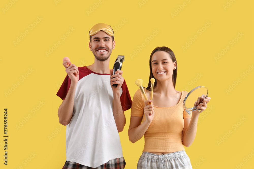 Young loving couple with trimmer and makeup accessories on yellow background