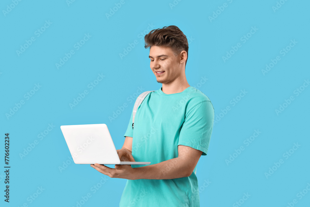 Male student using laptop on blue background