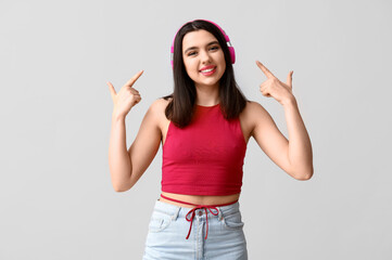 Wall Mural - Beautiful young woman pointing at modern headphones on grey background