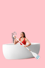 Poster - Female lifeguard with paddle in bathtub on pink background