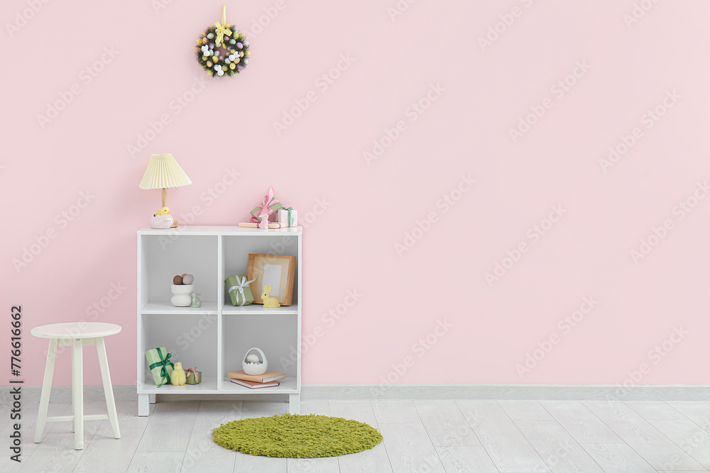 Beautiful Easter wreath decorated with eggs and table with shelving unit in room