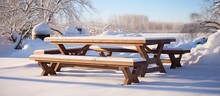 Snow Covers A Wooden Picnic Table Located Next To A Pile Of Snow In A Wintry Outdoor Setting