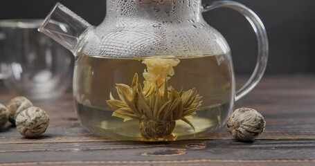 Wall Mural - Blooming flower tea ball brewing in a glass teapot with Hot boiling water on wooden background