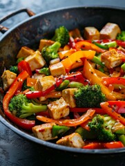 Sizzling vegetable stir-fry featuring golden tofu cubes and a medley of bright peppers, broccoli, and onions in a traditional wok, ready to serve.