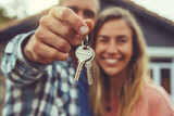 Fototapeta  - A happy young couple proudly holding keys to their new home, standing outside the property