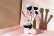 Set of professional make up brushes into the vase at beige background with shadow, modern cosmetic tools concept