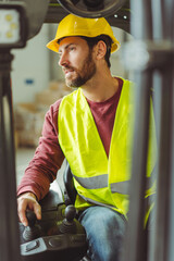 Wall Mural - Attractive man, operator, driver wearing hard hat, workwear drives forklift, working in warehouse