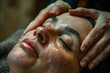 Beautiful woman having facial massage in spa salon, closeup photo of hands massaging face on table with closed eyes and dark hair lying down at luxury beauty center