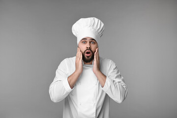 Wall Mural - Surprised young chef in uniform on grey background