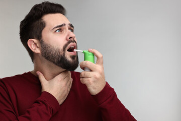 Sticker - Young man using throat spray on grey background. Space for text