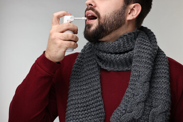 Sticker - Young man with scarf using throat spray on grey background, closeup