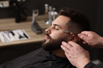 Poster - Professional barber shaving client's beard with blade in barbershop, closeup