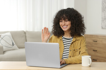 Wall Mural - Happy woman waving hello during video call at table in room