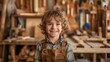 A smiling young child wearing overalls in a woodworking shop filled with tools, exuding a sense of joy and creativity.