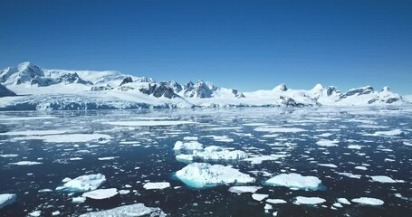 Wall Mural - Antarctica aerial panorama landscape in sunny day. Towering snow-covered mountains, blue clear sky reflect in polar ocean water. Icebergs melting under sun. Global warming climate change. Drone shot