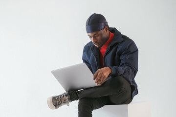 Wall Mural - Front view, with laptop. Black man in cap is in the studio against white background