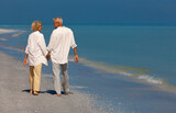 Fototapeta Big Ben - Happy senior couple walking smiling holding hands on an empty tropical beach