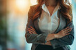 Woman's torso, gray blazer, folded arms, bright background, business vibe.
