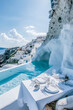A luxurious dining setup by a serene pool overlooking the iconic white architecture of Santorini, offering an exquisite experience