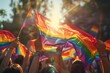 © Viktoriia - A crowd at a pride event waves rainbow flags with a warm sunset in the background, Vibrant pride parade celebration