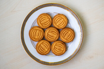 Tasty wheat biscuits filled with milk cream served on a white plate on wooden background. Top view