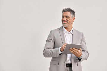 Happy mature business man using digital tablet isolated on white background. Middle aged ceo executive wearing suit, older businessman professional entrepreneur looking away at copy space.