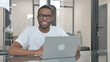 © stockbakers - Young African Man Smiling at Camera while Working on Laptop in Office