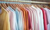Fototapeta  - Zbliżenie na równy rząd kolorowych, lekkich, letnich ubrań wiszących na drewnianych wieszakach w domowej szafie, w sklepie. Koncepcja handlu, kolekcjonowania odzieży.
