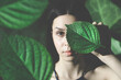 woman covering  half her face with a leaf surrounded by nature, concept of nature and life