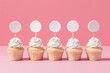 Five vanilla cupcakes with fluffy white frosting and blank circular toppers ready for customization, on a pink background.