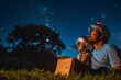 Father and Child Gazing at Stars in Astronaut Helmets. A father and his young child sitting on grass, wearing astronaut helmets, looking at the night sky filled with stars.