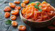 A bowl of candied orange slices garnished with fresh mint leaves on a dark textured background.