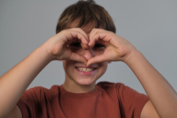 Wall Mural - Boy in a terra-cotta shirt forms a heart with his fingers, smiling sweetly. A beautiful reminder of the innocence and pure affection in childhood.