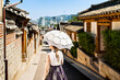 South Korea, Seoul. Woman in hanbok in Bukchon Hanok Village. Girl wearing traditional dress and costume. Korean tradition. City skyline in the background. Travel in summer or spring. Back view.